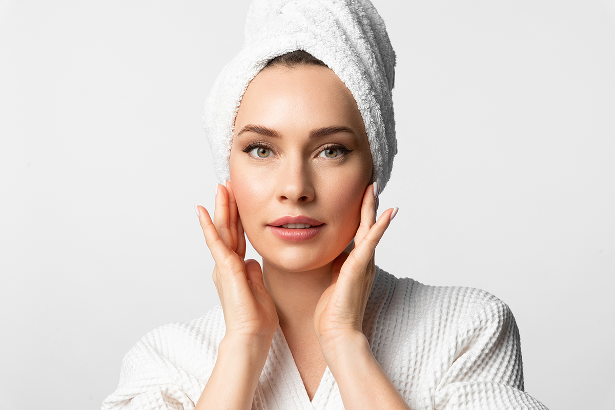A beautiful attractive woman in bath clothes applies moisturizer cream to her face