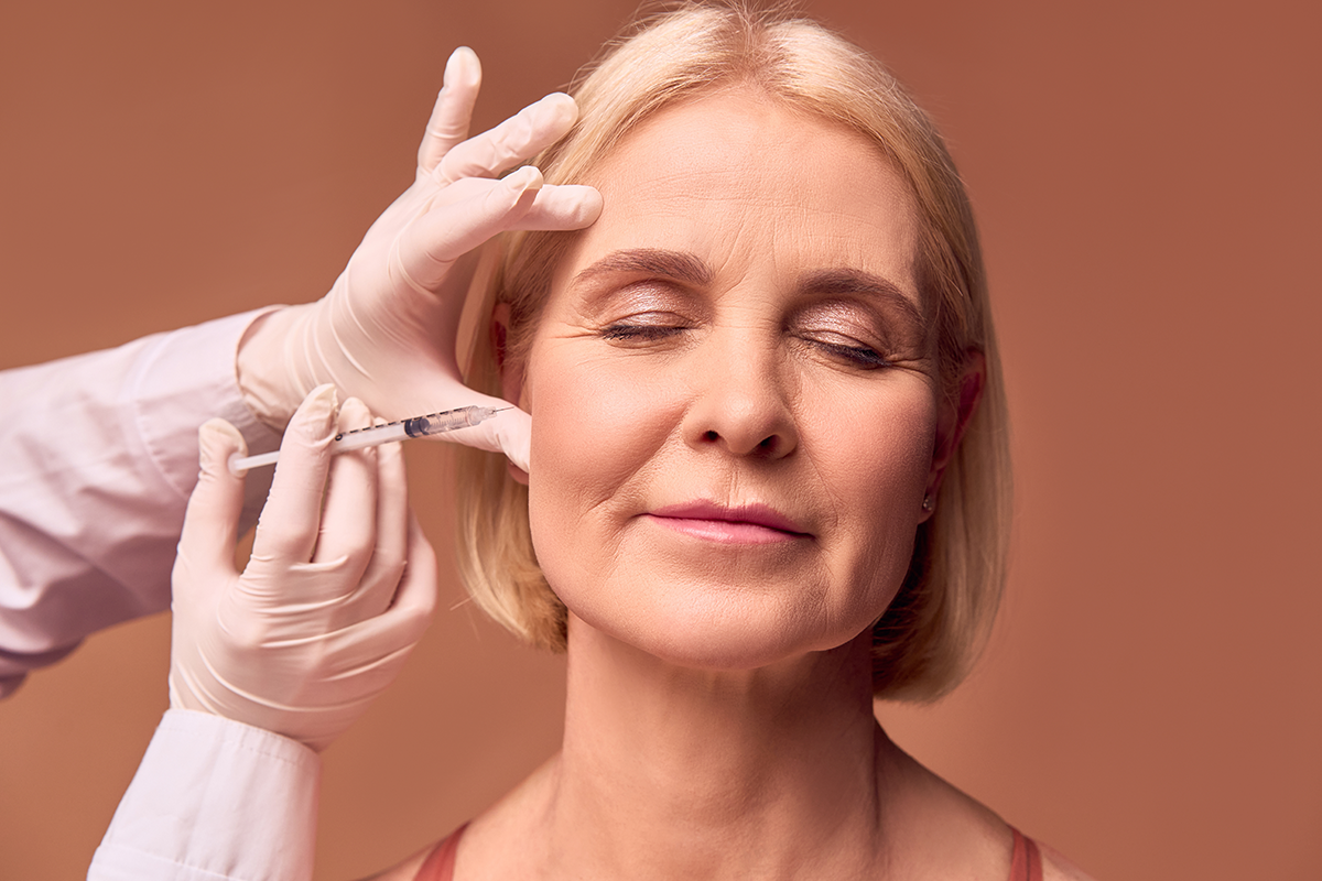 Hands in white gloves and a medical gown make an injection in the cheekbone
