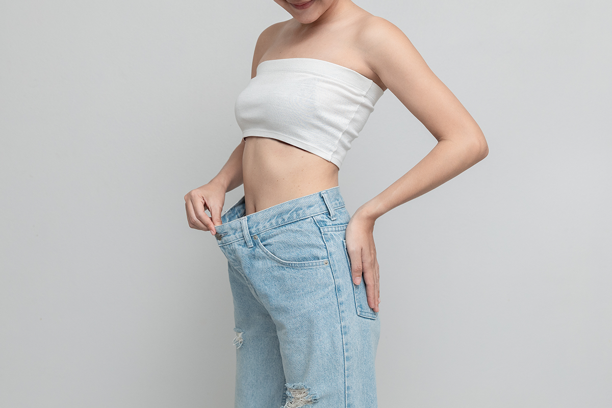 Happy woman is showing her old oversized jeans after successful diet