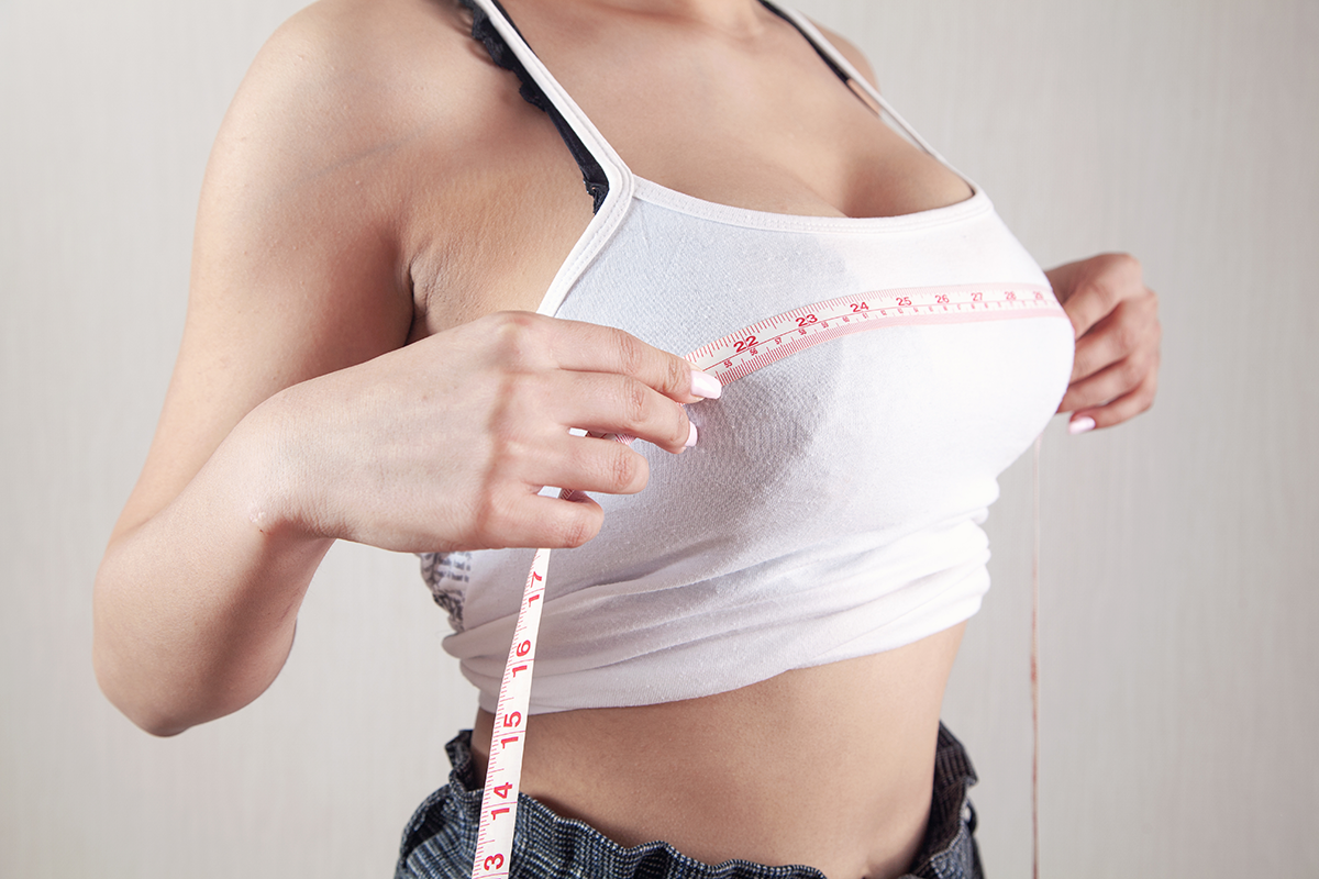 Young woman measures her breasts with a measuring tape
